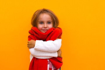 Funny little girl celebrating winter holidays peeking out from behind a red scarf on an isolated yellow background