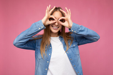 Photo of young positive happy smiling beautiful woman with sincere emotions wearing stylish clothes isolated over background with copy space and showing glasses gesture with hands