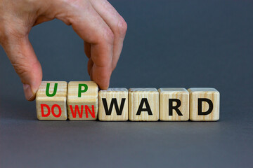 Upward or downward symbol. Businessman turns wooden cubes and changes the word 'downward' to 'upward'. Beautiful grey table, grey background. Business, upward or downward concept. Copy space.