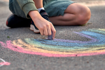 Kids paint outdoors. Boy drawing a rainbow colored chalk on the asphalt the playground
