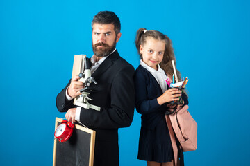 Father and pupil daughter ready to school. Portrait of dad and little girls with school supplies, isolated on blue background.