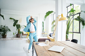 Happy cheerful young attractive business woman in formal suit dancing victory dance in home office. Female office worker having fun at work place.