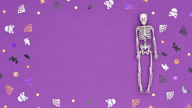 Halloween stop motion video 4K Loop. Three skeletons roll over a purple background decorated with confetti in the shape of skulls, spider webs, spiders, witches, pumpkins and bats. 