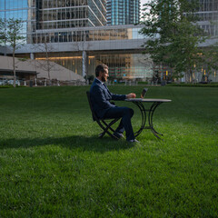 Fototapeta premium Middle aged businessman typing on laptop computer sitting at table on office terrace. Man working remotely in modern park.