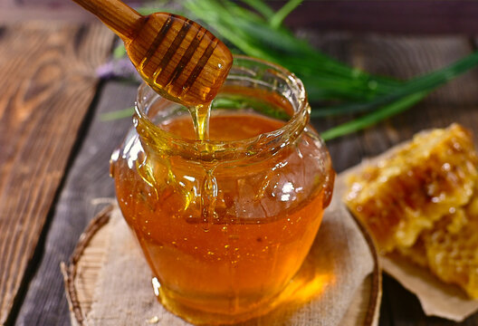 Fresh honey in a glass jar next to the honeycomb on the table. A wooden spoon with dripping honey. World Bee and Honey Day. Beekeeping. Healthy food
