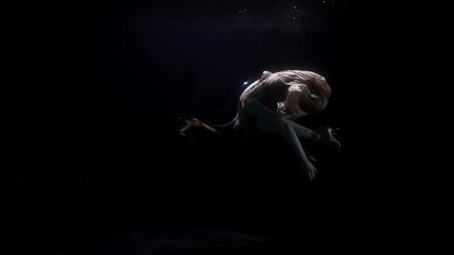 graceful woman is floating underwater, keeping afloat in fetal position