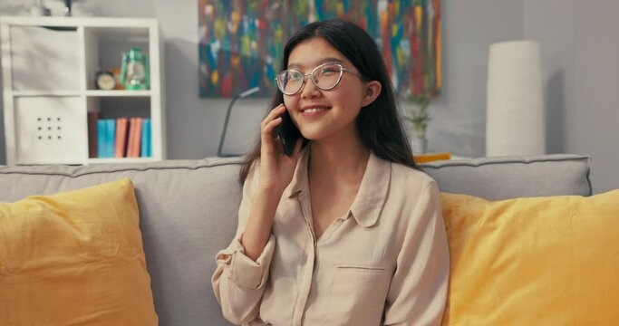 Smiling girl of characteristic beauty is sitting on sofa talking on phone she receives information about promotion, winning award, concours, getting into her dream university, scholarship she is happy