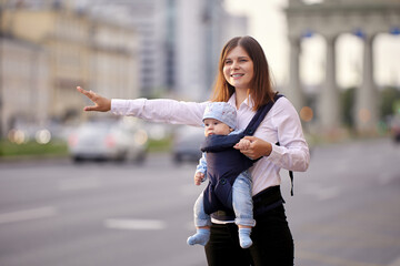 Happy young mother with baby in sling is stopping taxi.