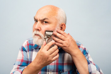 Old gray man cut bear with hair clipper. Portrait of barber hold old razor hair clipper, vintage barber shop, shaving. Old bearded man. Vintage barbershop.