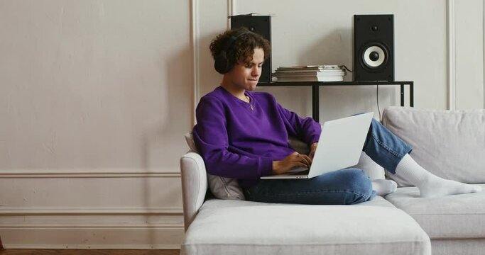 Handsome guy in casual clothes and headphones uses laptop enjoying and singing