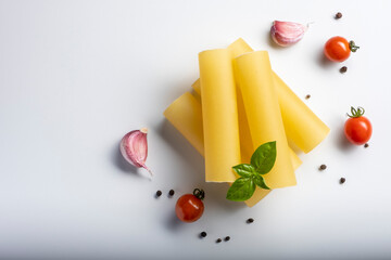 Raw cannelloni pasta on white background with cherry tomatoes, garlic and basil.