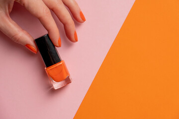 Woman hand hold orange lacquer on orange pink background. Female hand with orange nail.