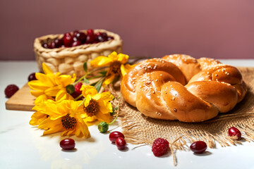 bun with sesame seeds on a white table next to yellow heliopsis flowers and a wicker basket with hawthorn