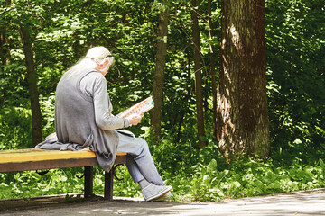 senior woman sitting on a park bench reading a book