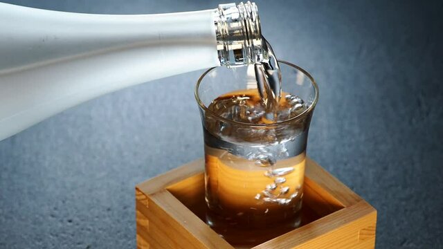 Tokyo,Japan - September 26, 2021: Pouring Sake into a glass inside a wooden measuring box or sake masu. This style is called as Mokkiri or Morikiri or Morikoboshi.
