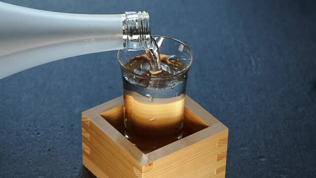 Tokyo,Japan - September 26, 2021: Pouring Sake into a glass inside a wooden measuring box or sake masu. This style is called as Mokkiri or Morikiri or Morikoboshi.

