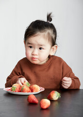 Asian little girl eating fruits, indoor white background