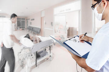 Doctor writing clipboard for diagnosis and medical active staff pushing stretcher gurney bed in labour room of hospital corridor with female patient pregnant in emergency status