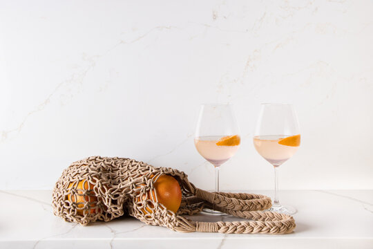 A couple of cocktail drinks and a bag of grapefruits being placed on a kitchen countertop which was made of white quartz stones