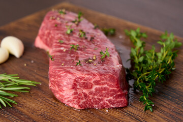 Raw marble striploin steak with thyme, rosemary, garlic, salt, pepper. Rustic beef tenderloin meat on wooden chopping board. Side view closeup horizontal
