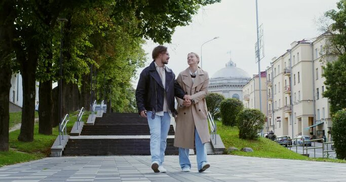 Stylish guy and girl are walking around the city, holding hands and talking