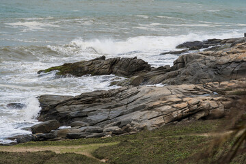 View of the beach of Rio das Ostras in Rio de Janeiro with sunny day, blue sky and some clouds. Strong sea and yellowish sand and lots of rocks.