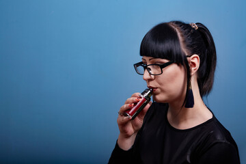 A beautiful girl with dark hair and glasses exquisitely smokes an electronic cigarette