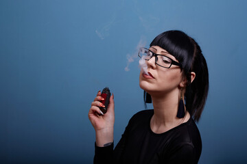 A beautiful girl with dark hair and glasses exquisitely smokes an electronic cigarette