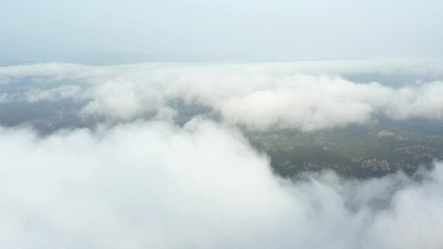 View from above, drone point of view, stunning aerial video of a drone flying over some fluffy moving clouds with a valley in the distance.