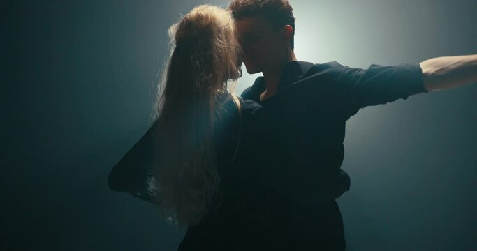 A professional dancer approaches a beautiful blonde girl, climbs up on toes, raises hands, their faces touch, the man turns partner, they smile gently, the girl overlaps the man from behind