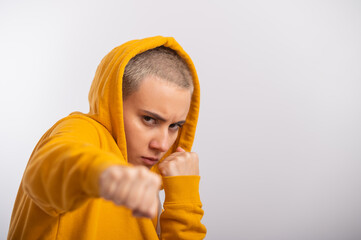 Young woman in ocher hood holding fists near face on white background. Boxer girl is ready for a...
