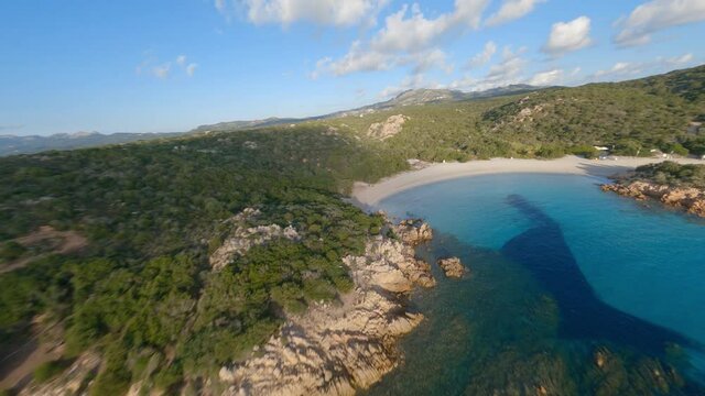 FPV video, view from above, aerial view from an FPV drone flying at high speed over a green coast with a beautiful white sand beach bathed by a turquoise water. Prince Beach (Spiaggia del Principe)