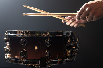 Snare drum and drummer's hands hitting drumsticks against a dark background.