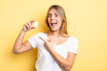 pretty blonde girl looking excited and surprised pointing to the side. pills bottle concept