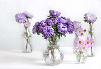 Glass vases with fresh chrysanthemum flowers on a blurred white background.