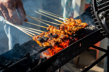 Chicken satay on traditional charcoal fire. satay on fire with smoke and an appetizing look. hands cooking satay on the grill