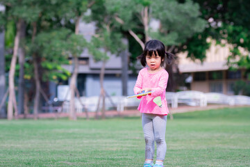 A 4-5 year old cute girl is trying to hit a badminton ball, Happy child is having fun practicing the sport. Summer time. Kid wearing pink t-shirt and gray leggings sweet smile. Hobby activity.