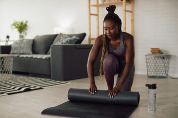 Black athletic woman unrolls exercise mat while preparing for home workout.