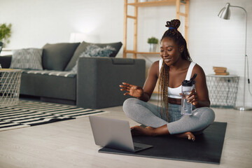 Fototapeta na wymiar Happy black athletic woman talks during video call over laptop while exercising at home.