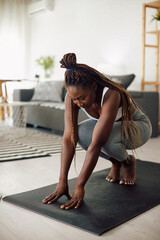 Young African American sportswoman does relaxation exercises during home workout.