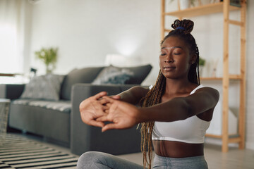 Black female athlete does breathing exercises while practicing Yoga at home.