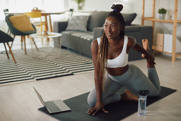 Young African American sportswoman stretches while warming up during online exercise class at home.