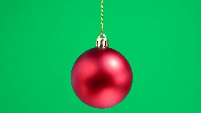Red matte christmas toy ball is spinning on a green plain background