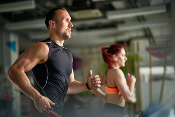 Fototapeta na wymiar Muscular build athlete runs on treadmill in gym.