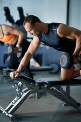 Athletic man lifts weights on bench during strength training in gym.