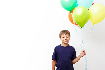 Fototapeta na wymiar Happy eight year old boy with an armful of bright colorfull balloons celebrates birthday.