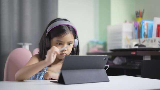asian child student or kid girl learning art drawing or write on computer tablet by touch pen on touch screen and wearing headset for video call or person learn from home school by study online class