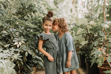 Two beautiful little girls of different nationalities walk in the botanical garden surrounded by tropical leaves and keep secrets. High quality photo