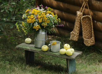 Still life with flowers in a jug and yellow apples in the garden.