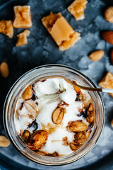 ice cream with caramel sauce and ground nuts served in a glass jar on a blue tray, vertical image. top view. place for text